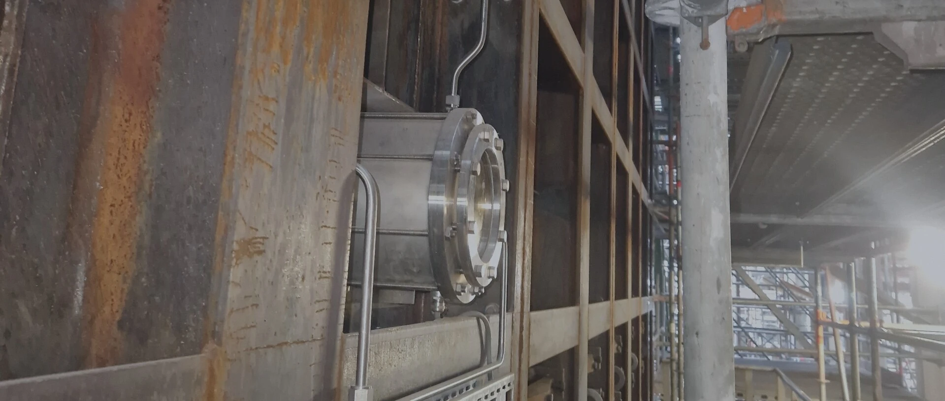 Bildbeschreibung: Eine industrielle Infrastruktur mit einem metallischen Rohr und rostigen Wänden in einem Bau- oder Fabrikgelände.