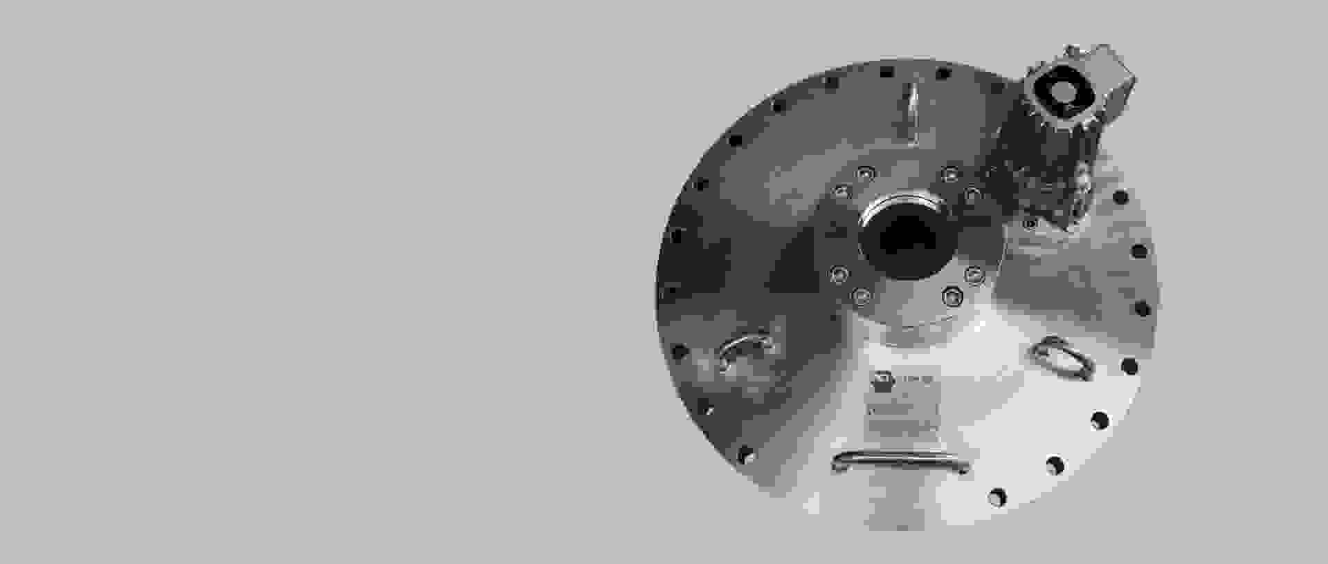 Eine metallische Platte mit einem zentralen Loch, Bolzen und einer kleinen Motorvorrichtung auf der Oberseite.