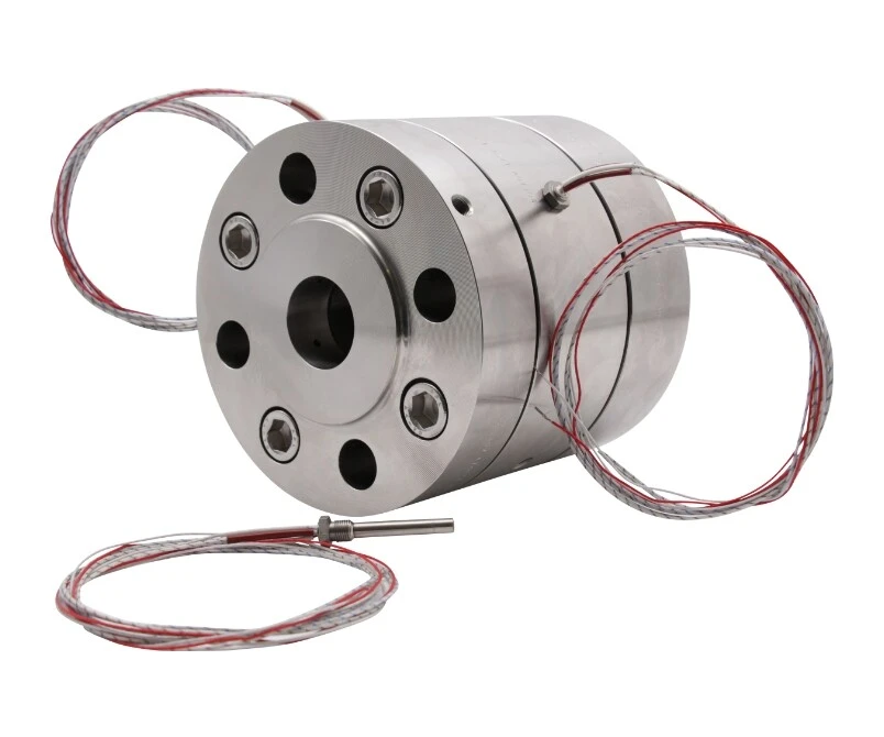 Ein metallisches Bauteil mit runder Form, mehreren Bohrungen und angeschlossenen Drähten. Es könnte sich um einen Sensor oder eine Verbindungseinheit handeln.