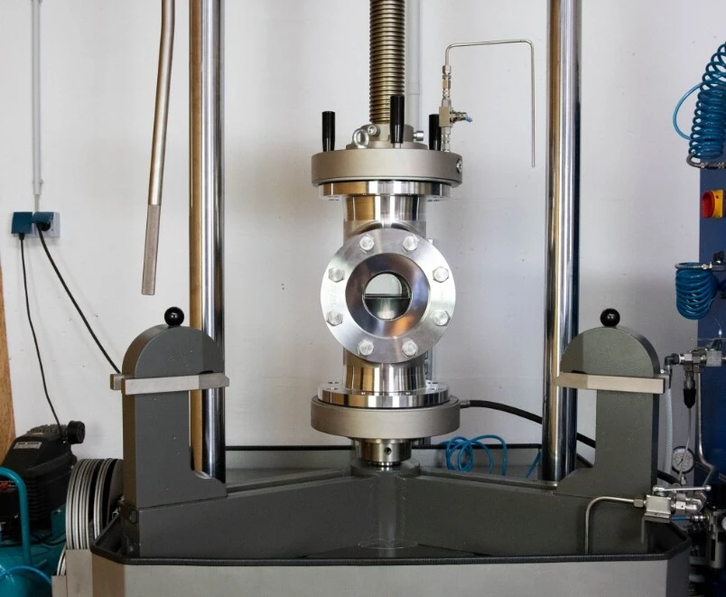Eine industrielle Maschine mit einem Metallrahmen und einem zentralen Zylinder. Sie zeigt Druck- und Steuerungsmechanismen.