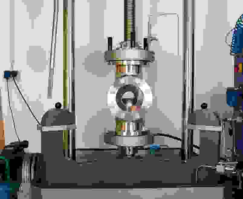 Eine industrielle Maschine mit einem Metallrahmen und einem zentralen Zylinder. Sie zeigt Druck- und Steuerungsmechanismen.