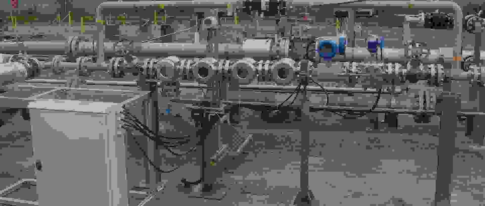 Several metal pipes and valves that are part of an industrial piping system, with a control box in the foreground.