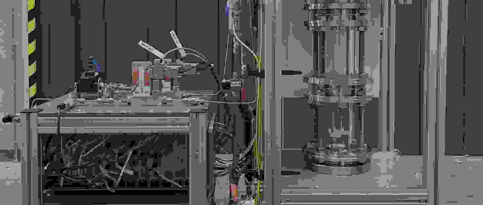 A technical device with two main parts: on the left, a control unit with pipes and sensors; on the right, a transparent pressure vessel system.