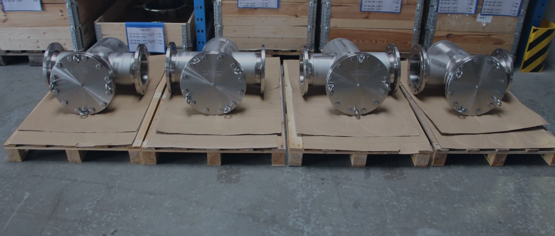 Several stainless steel components in a warehouse, placed on wooden pallets.