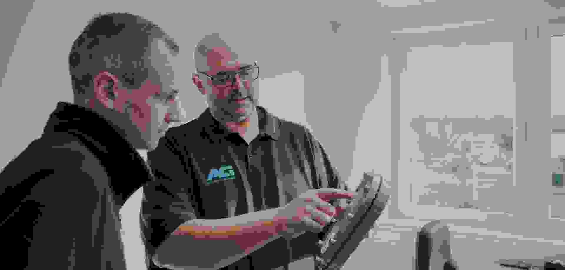 Two men discussing an industrial component – one pointing at a round metal housing with sight glass.
