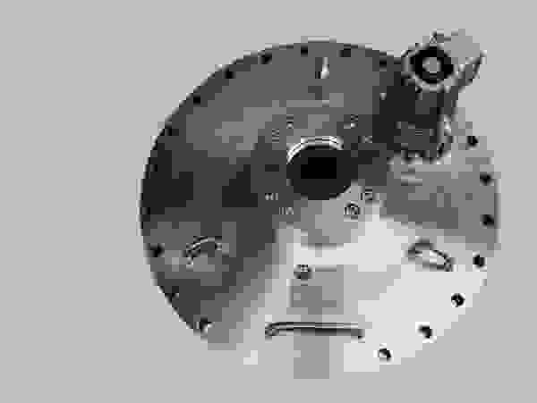 A metallic plate with a central hole, bolts, and a small motor device on top.