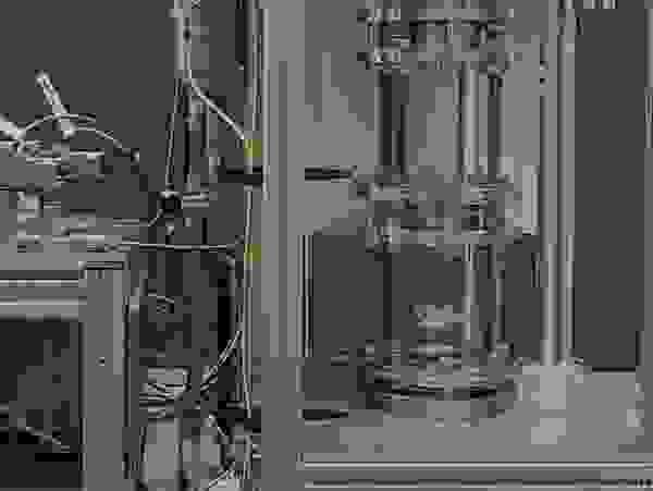 A technical device with two main parts: on the left, a control unit with pipes and sensors; on the right, a transparent pressure vessel system.