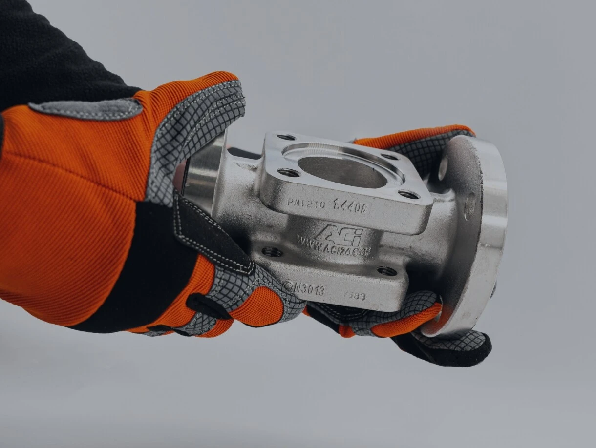 Someone is holding a custom-made fitting from ACI in their hands, wearing gloves.