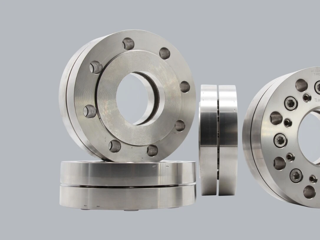 Stainless steel machine parts, including various pulleys and flanges, on a grey background.