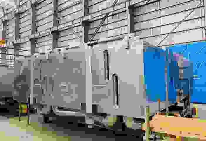 Groot industrieel metalen apparaat met een zilveren en blauwe kleur, opgeslagen in een hal.