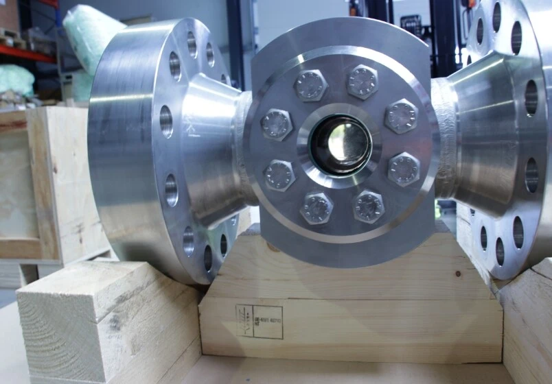 Een metalen buisverbinding met flenzen, vastgezet op een houten blok.