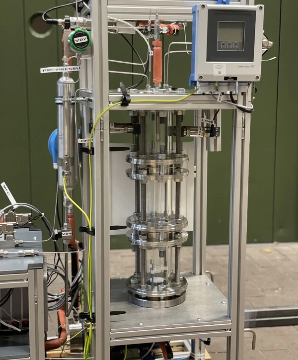 Een metalen apparaat met transparante cilinders en verschillende sensoren, waarschijnlijk een proefopstelling of een druktestbank.