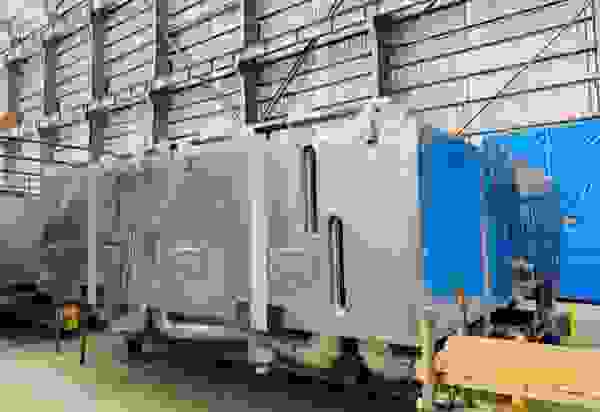Groot industrieel metalen apparaat met een zilveren en blauwe kleur, opgeslagen in een hal.