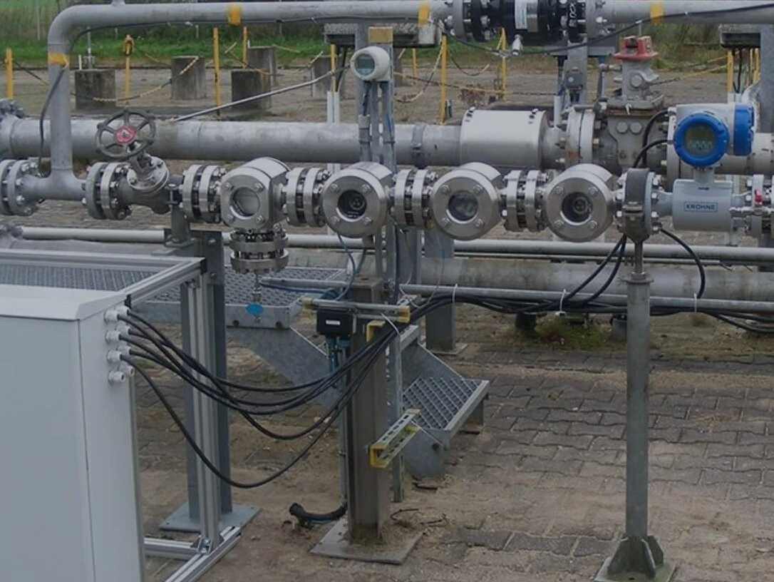 Meerdere metalen leidingen en ventielen die deel uitmaken van een industriële pijpleidinginstallatie, met een controlekast op de voorgrond.