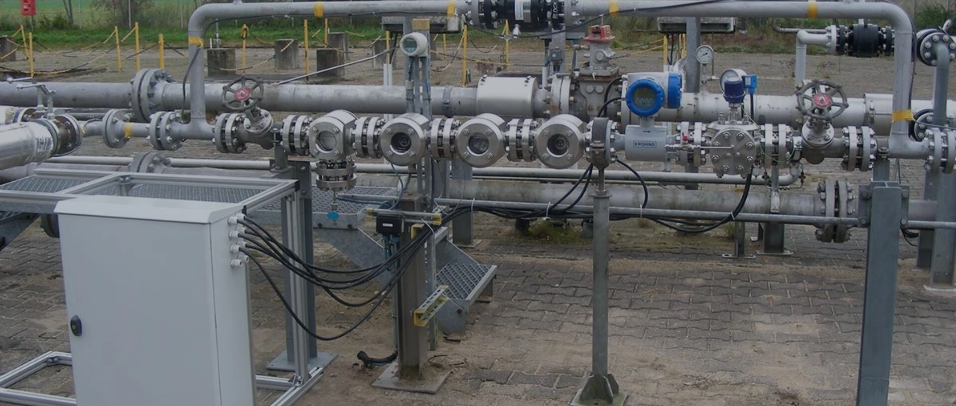 Kilka metalowych rur i zaworów, które są częścią przemysłowej instalacji rurociągowej, z skrzynką kontrolną na pierwszym planie.